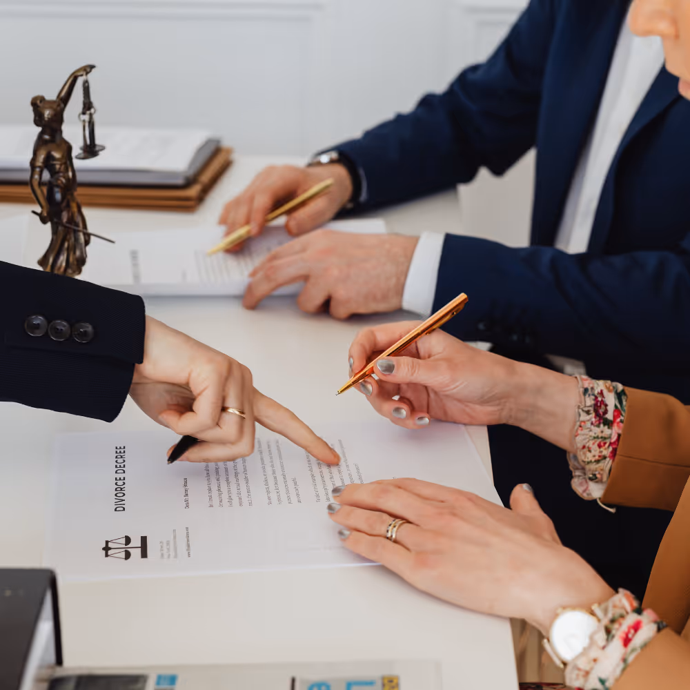 Close-up of two people reviewing and signing a divorce decree document at a desk with a small statue of Lady Justice.
