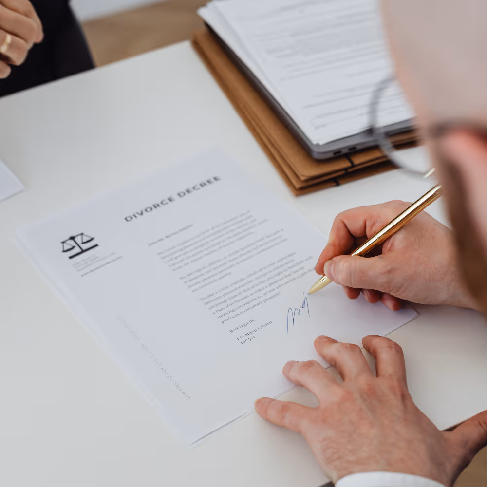 Person signing a divorce decree document on a white desk with a pen.